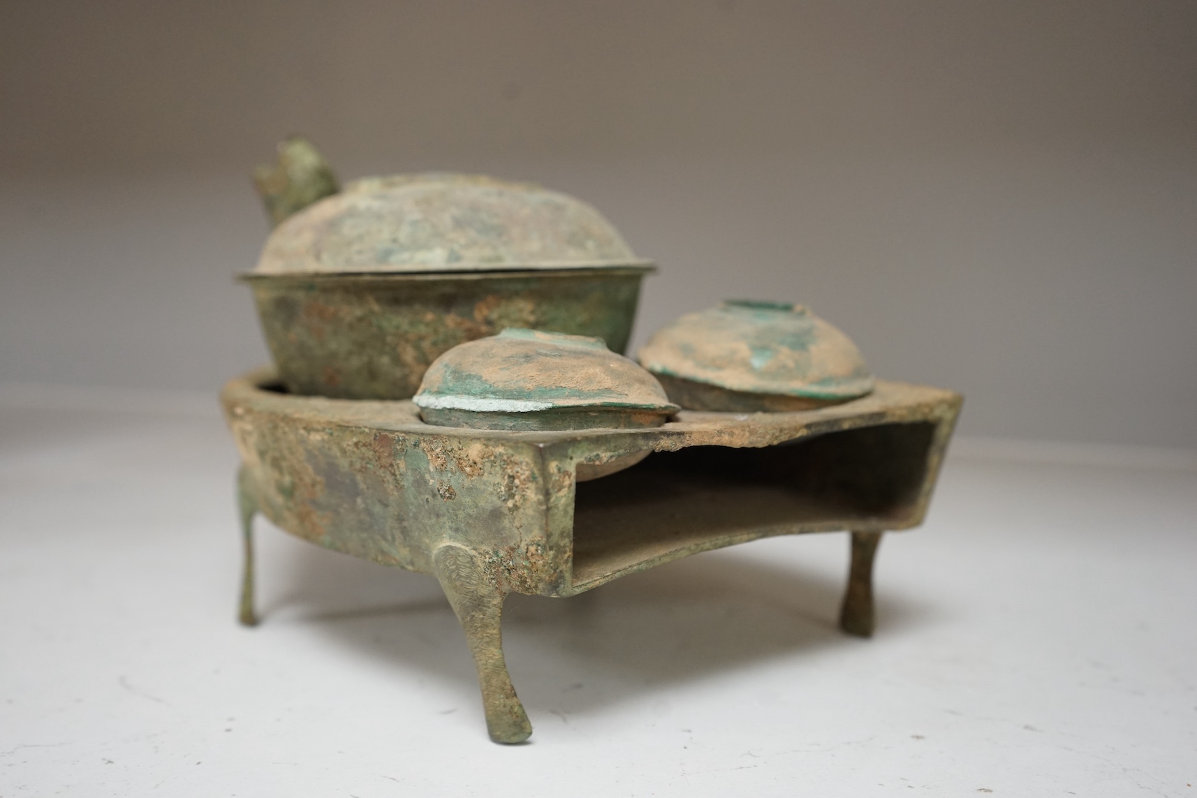 Four Chinese bronze zoomorphic stoves, Han Dynasty, 22cm, together with a Han Dynasty bronze brazier and vessels, width 22.5cm, (5). Condition - poor to fair.